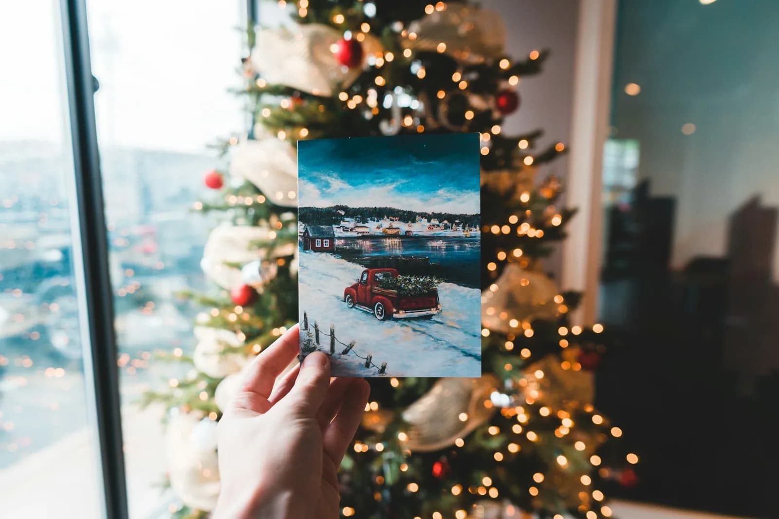 Ruka drži ispisanu fotografiju ispred okićenog božićnog drvca s lampicama