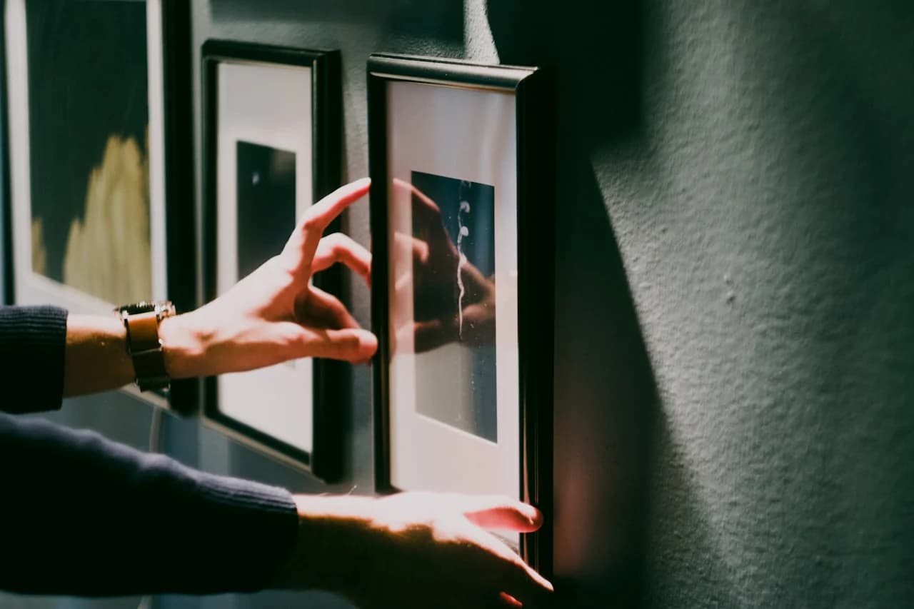 Mlada osoba slaže kvadratne fotografije u simetričnu mrežu na zidu