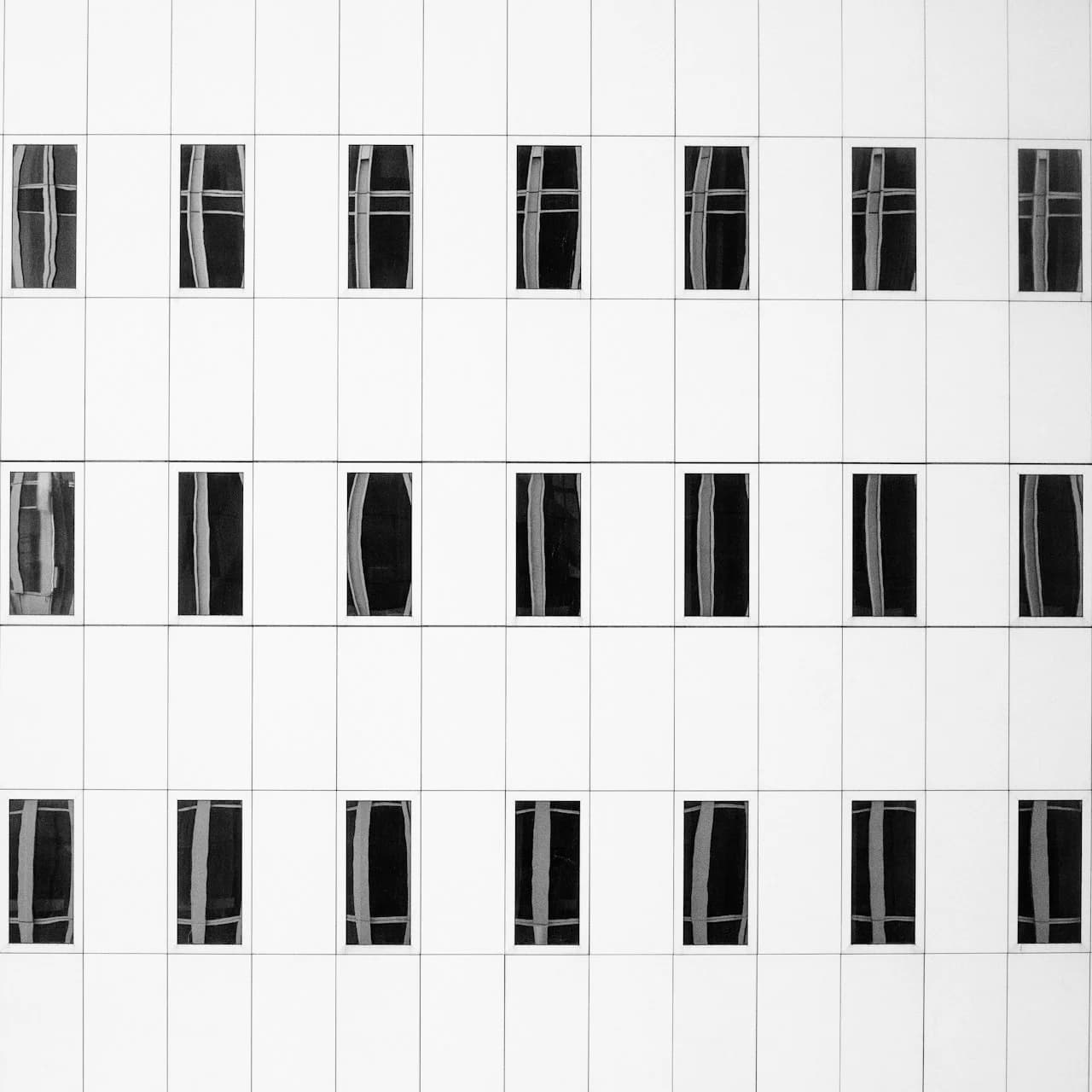Kvadratne fotografije 15 × 15 cm u simetričnoj mreži na bijelom zidu