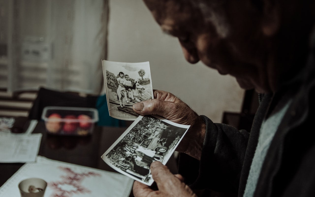 Stariji muškarac u rukama drži dvije stare crno-bijele fotografije