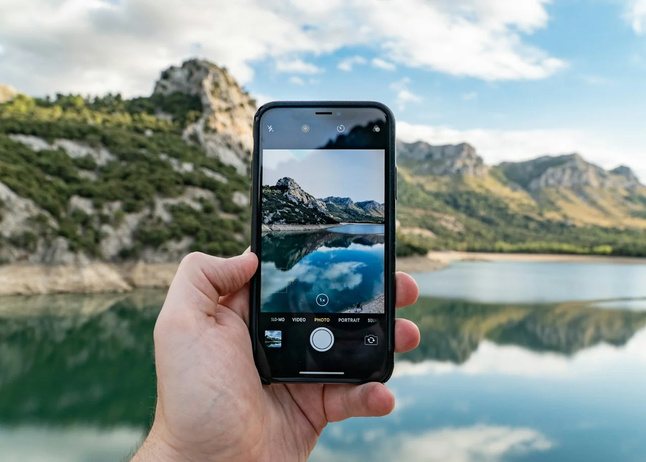 Ruka drži mobitel, na zaslonu je snimka jezera i planina