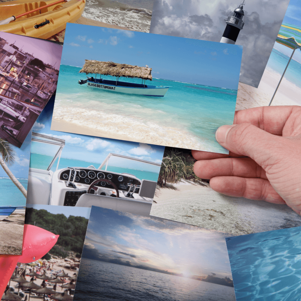 Roka drži natisnjeno fotografijo tropske plaže z ladjo med drugimi potovalnimi fotografijami